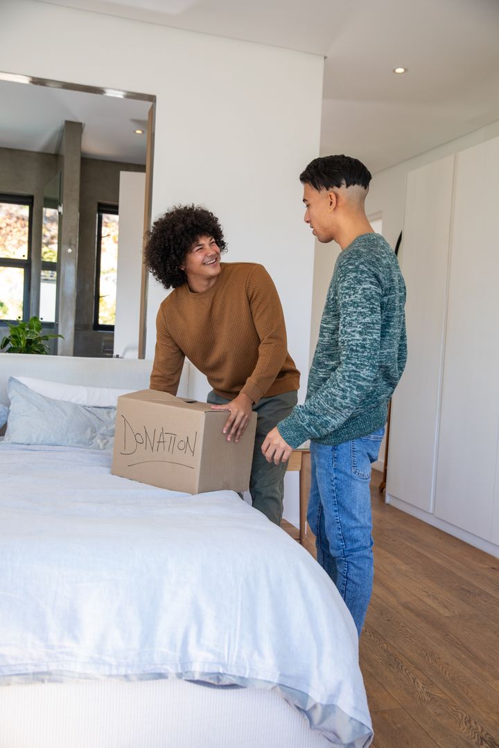 Two Men Collaborating on Donation Box Arrangement in Modern Bedroom