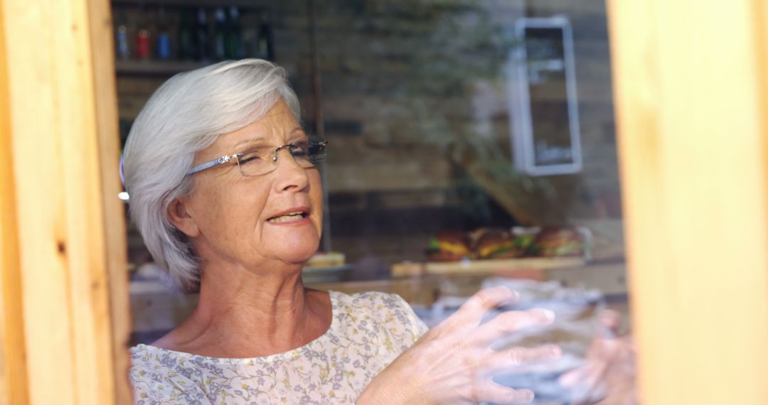 A senior Caucasian woman looks thoughtfully out of a window, with copy space - Free Images, Stock Photos and Pictures on Pikwizard.com