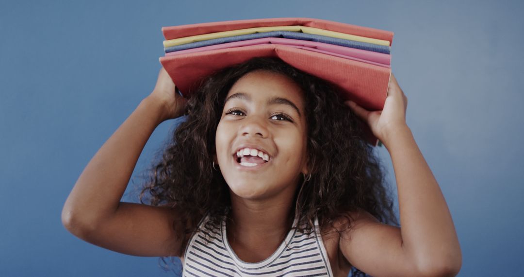 Happy African American Girl Holding Stack of Books on Her Head - Free Images, Stock Photos and Pictures on Pikwizard.com