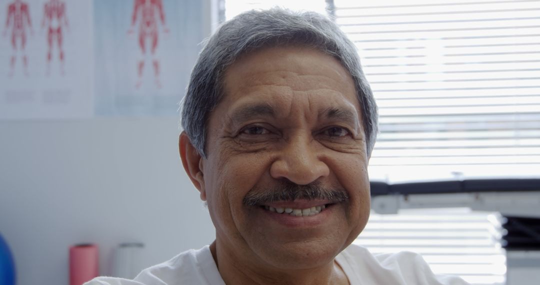 Elderly Man Smiling in Medical Office with Anatomy Charts in Background - Free Images, Stock Photos and Pictures on Pikwizard.com