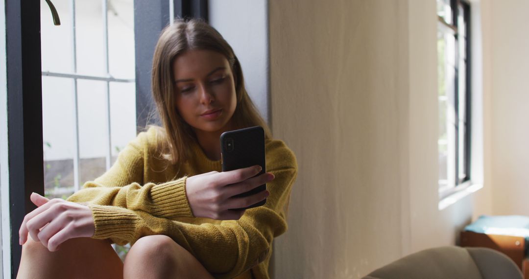 Young Woman Relaxing and Using Smartphone Near Window - Free Images, Stock Photos and Pictures on Pikwizard.com