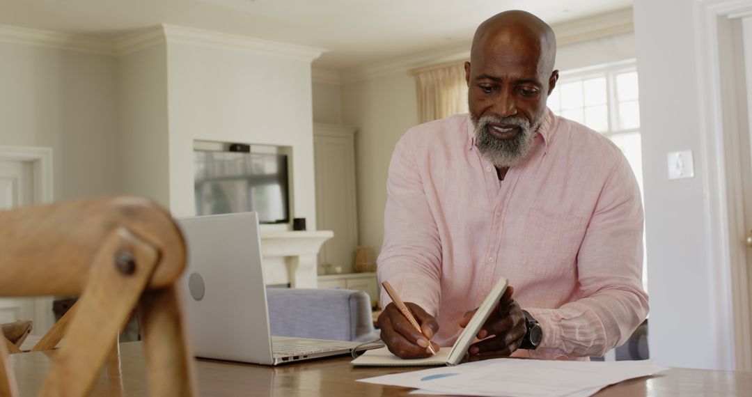Senior Man at Home Focusing on Work with Laptop and Notebook