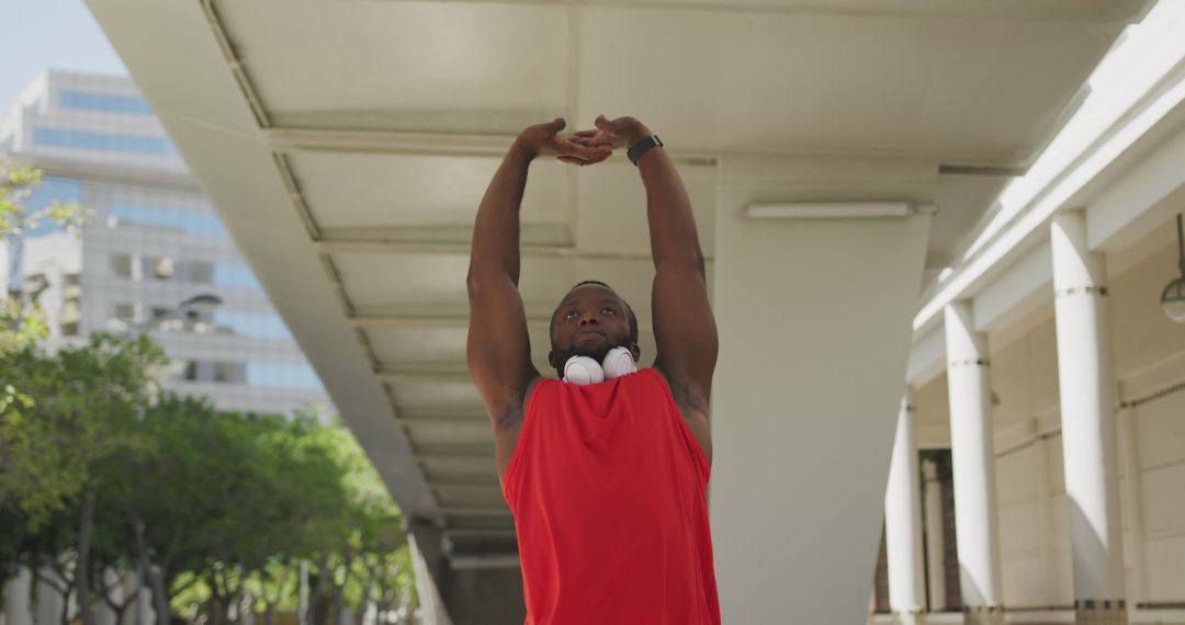 Young African American man stretching with headphones, outdoor urban setting - Free Images, Stock Photos and Pictures on Pikwizard.com