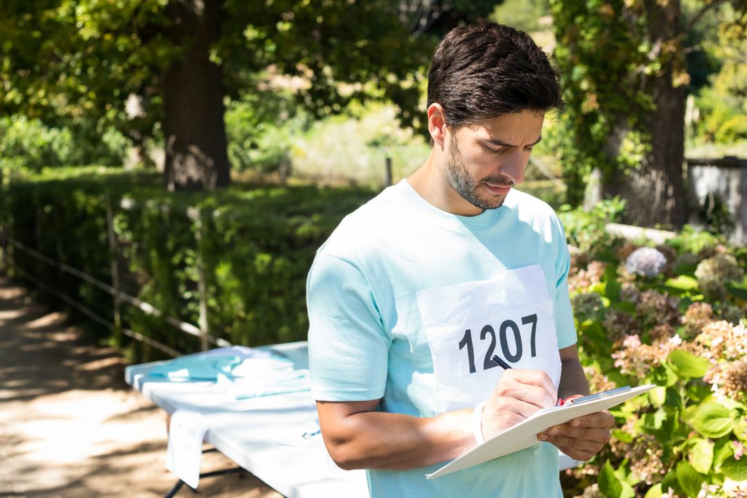 Male Volunteer Recording Data at Outdoor Event with Greenery