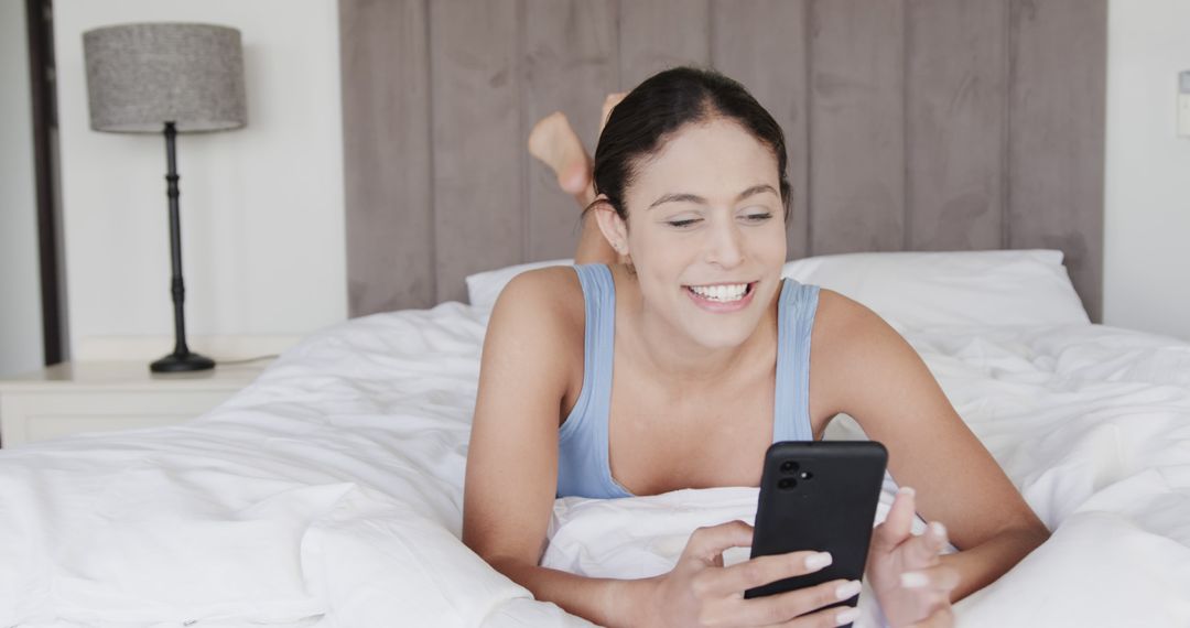 Woman Relaxing on Bed Using Smartphone Smiling Happily - Free Images, Stock Photos and Pictures on Pikwizard.com