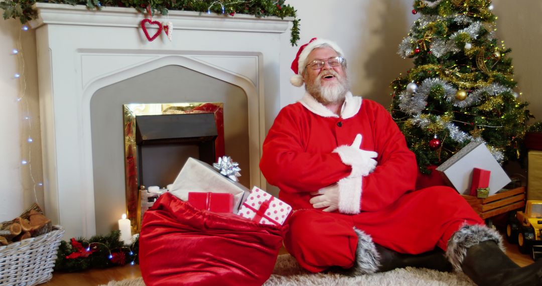 Santa Claus Joyfully Sitting by Christmas Tree with Gifts and Fireplace - Free Images, Stock Photos and Pictures on Pikwizard.com