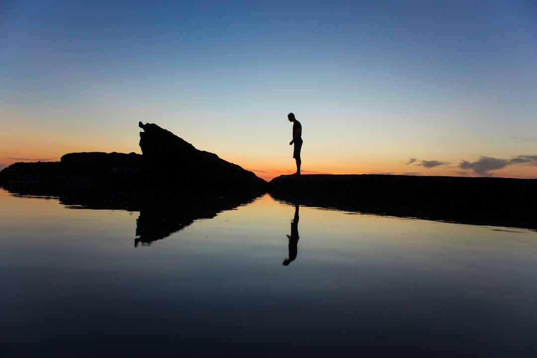 Silhouette of Man Standing Near Body of Water during Yellow Sunset - Free Images, Stock Photos and Pictures on Pikwizard.com