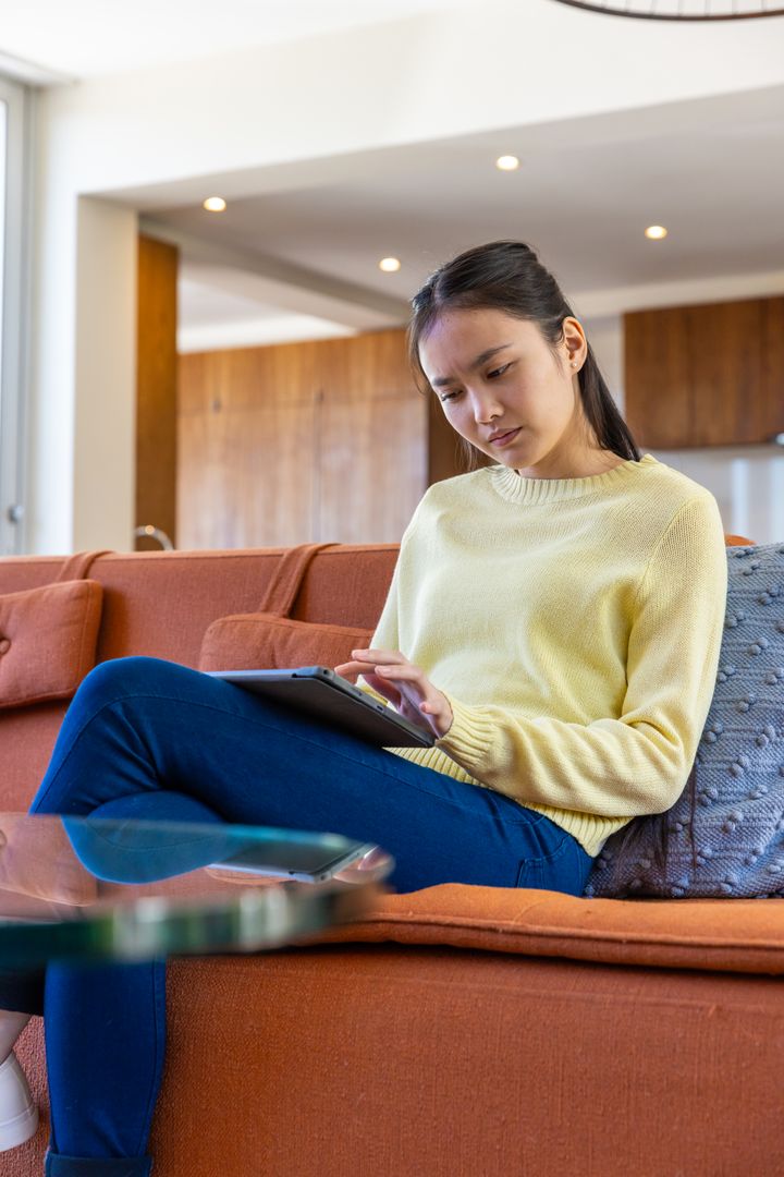 Asian Woman Relaxed on Couch Using Tablet in Modern Minimalist Home