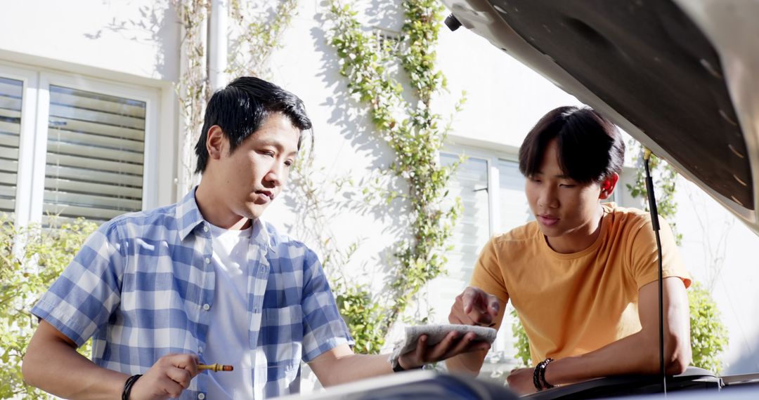 Father and Son Inspecting Car Engine Together in Use of Tablet