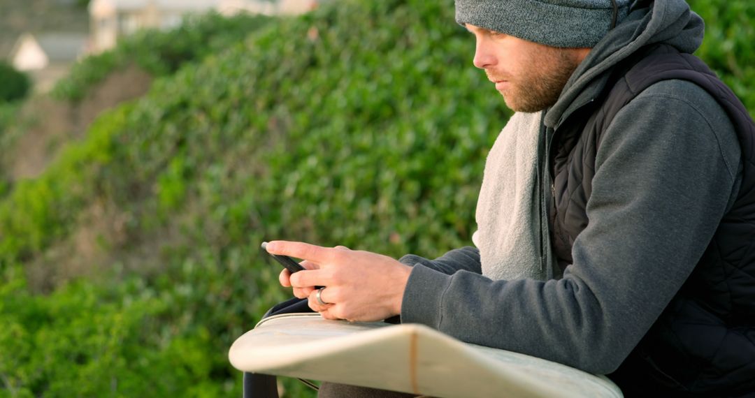 Man Checking Smartphone While Sitting Outdoors Beside Surfboard - Free Images, Stock Photos and Pictures on Pikwizard.com