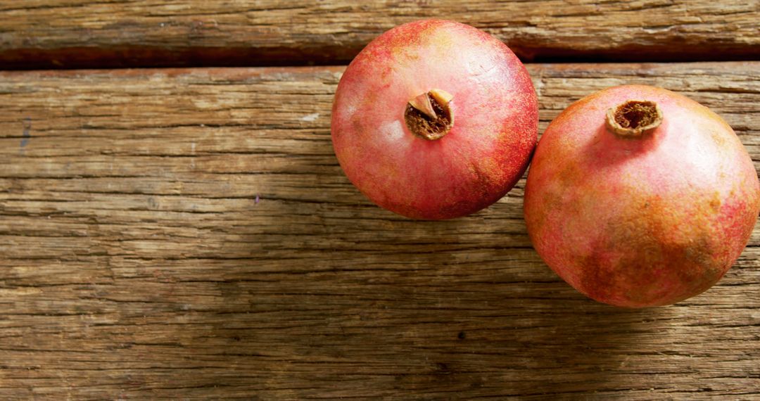 Two ripe pomegranates rest on a rustic wooden surface, showcasing their vibrant red skin - Free Images, Stock Photos and Pictures on Pikwizard.com