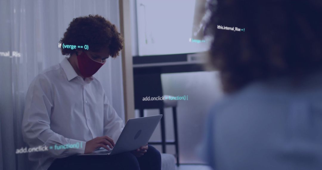 Young professional wearing red face mask typing on laptop with floating code overlay
