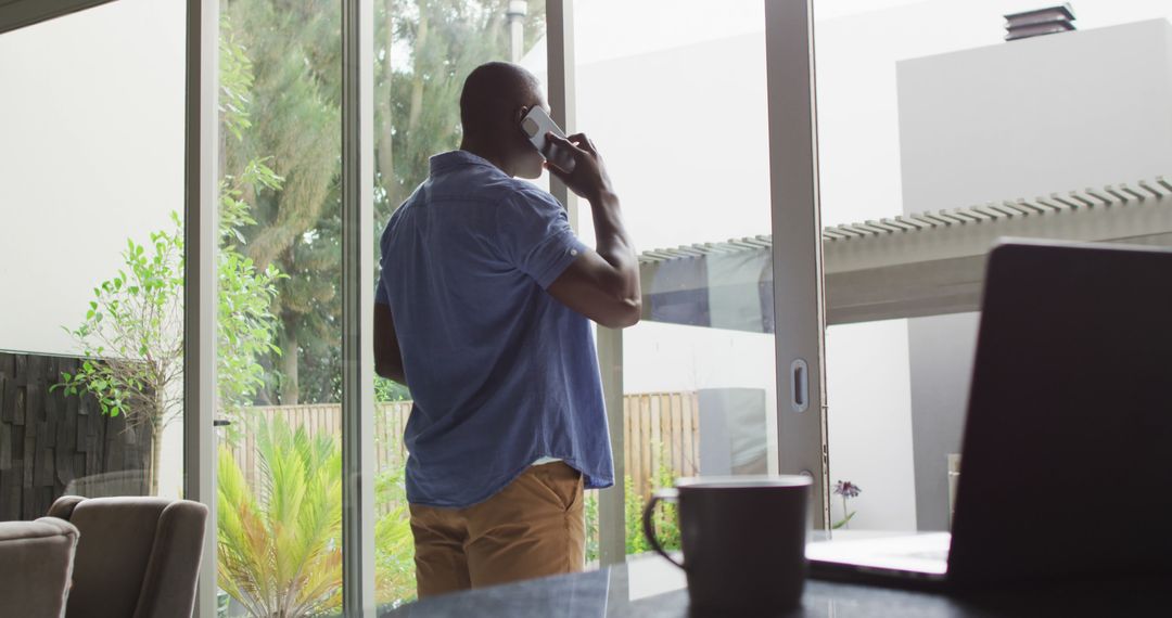 Man talking on phone standing near large sliding glass doors - Free Images, Stock Photos and Pictures on Pikwizard.com