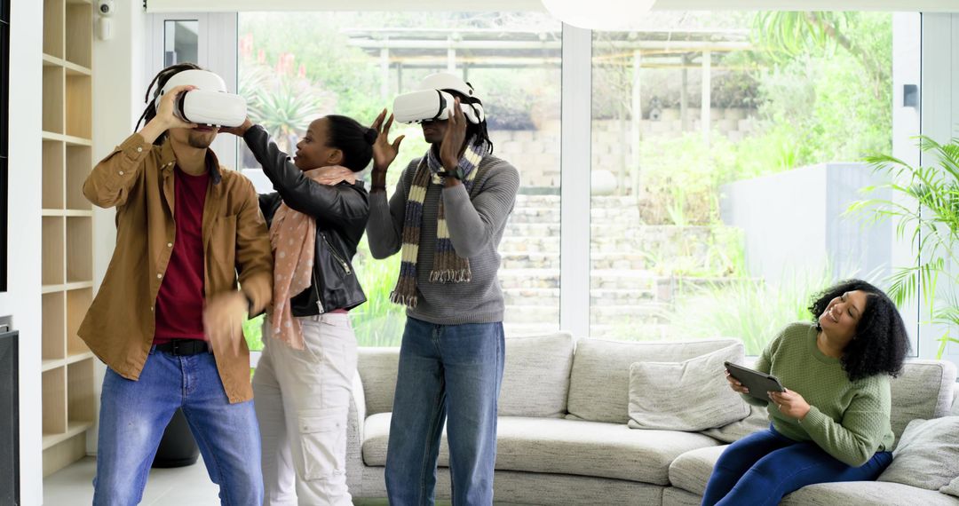 Diverse friends testing VR headsets in sunlit living room while companion using tablet