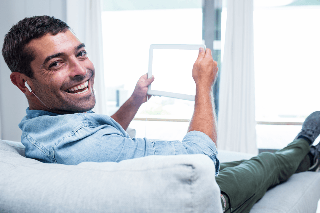 Young Man Smiling on Couch Holding Transparent Tablet Screen