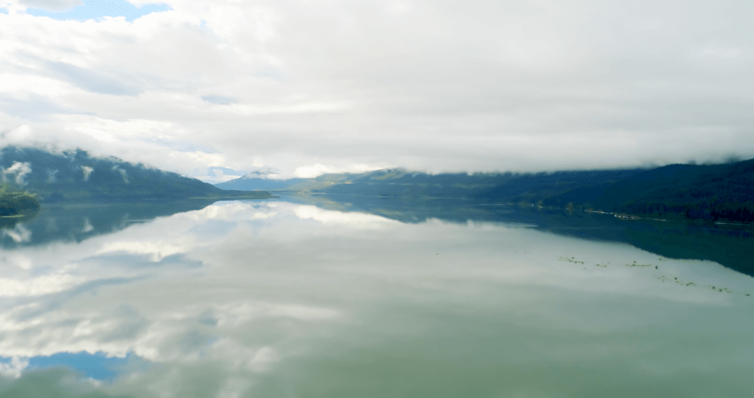 Transparent Lake Reflection with Lush Mountains and Cloudy Sky