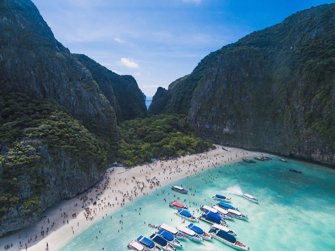Boats Docking in Turquoise Cove Flanked by Towering Limestone Cliffs, Crowded Beach