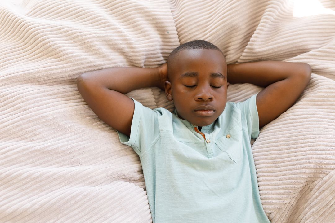 Close up of an african american boy lying in bed with eyes closed and arms behind his head - Free Images, Stock Photos and Pictures on Pikwizard.com