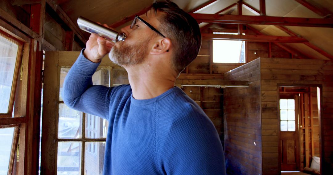 Man Drinking from Flask in Rustic Cabin Interior - Free Images, Stock Photos and Pictures on Pikwizard.com