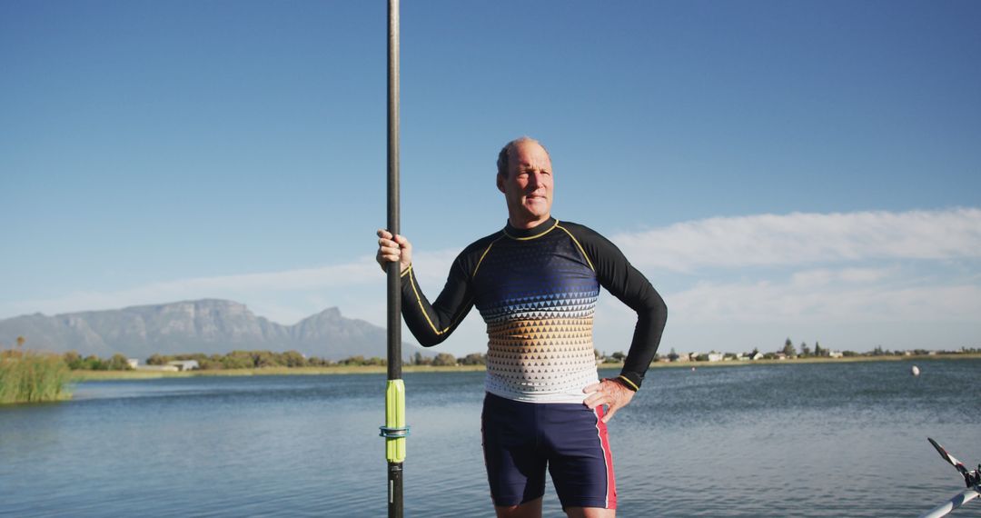 Confident athlete with kayak paddle standing by serene lake on sunny day - Free Images, Stock Photos and Pictures on Pikwizard.com