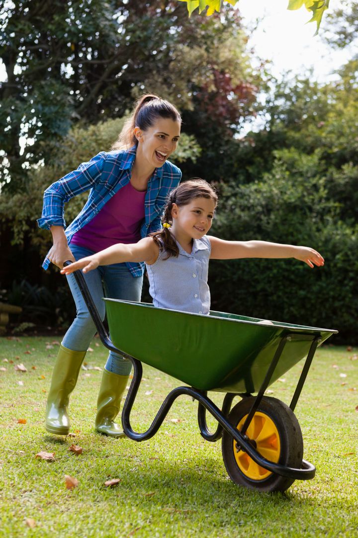 Cheerful Mother Pushing Daughter in Wheelbarrow in Backyard - Free Images, Stock Photos and Pictures on Pikwizard.com