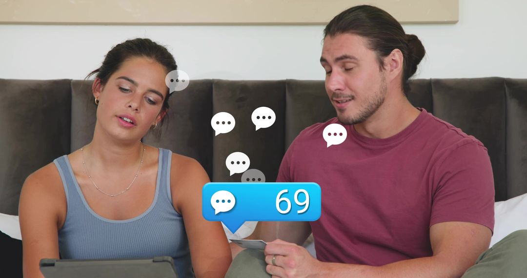 Young couple browsing tablet in cozy bedroom, reacting to 69 message notification