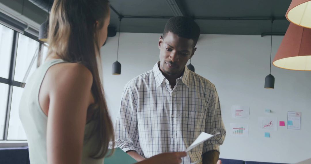 Colleagues collaborating over documents in modern office corner with charts and daylight