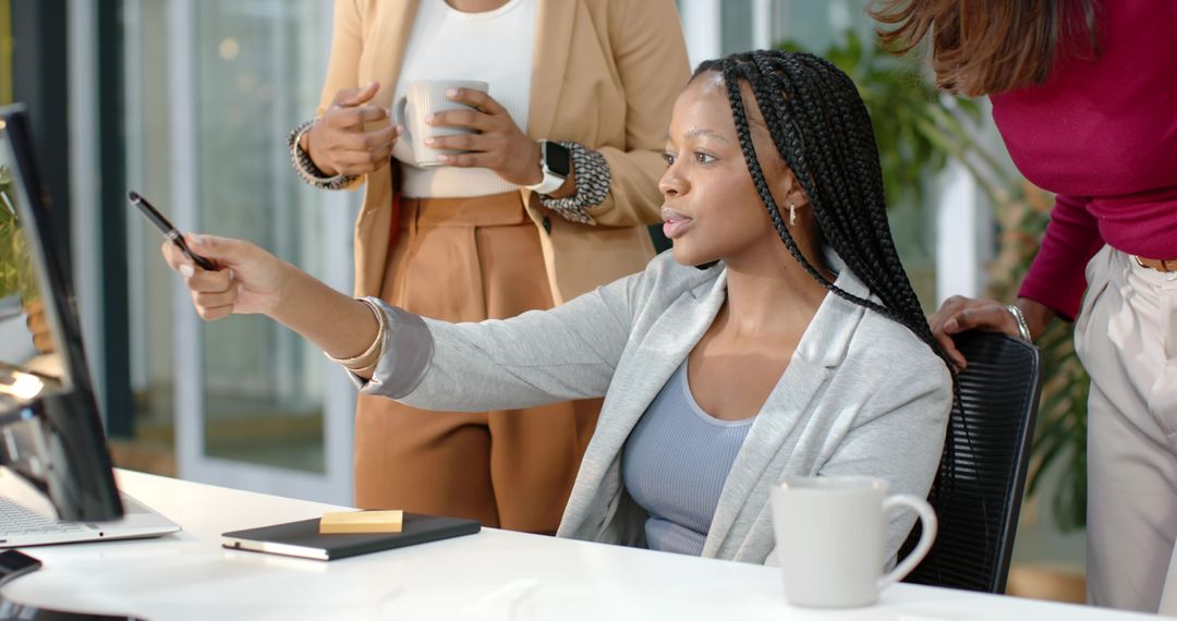 Diverse female team collaborating at desk pointing at monitor during brainstorming session
