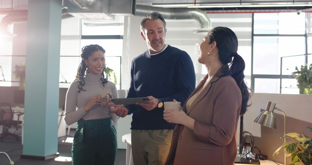 Diverse Team Collaborating in Open-Plan Office Holding Tablet and Coffee During Huddle
