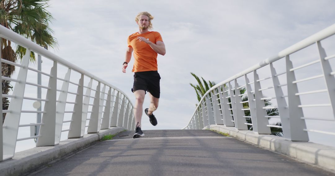 Blonde Man Running on Bridge for Fitness in Orange Shirt - Free Images, Stock Photos and Pictures on Pikwizard.com