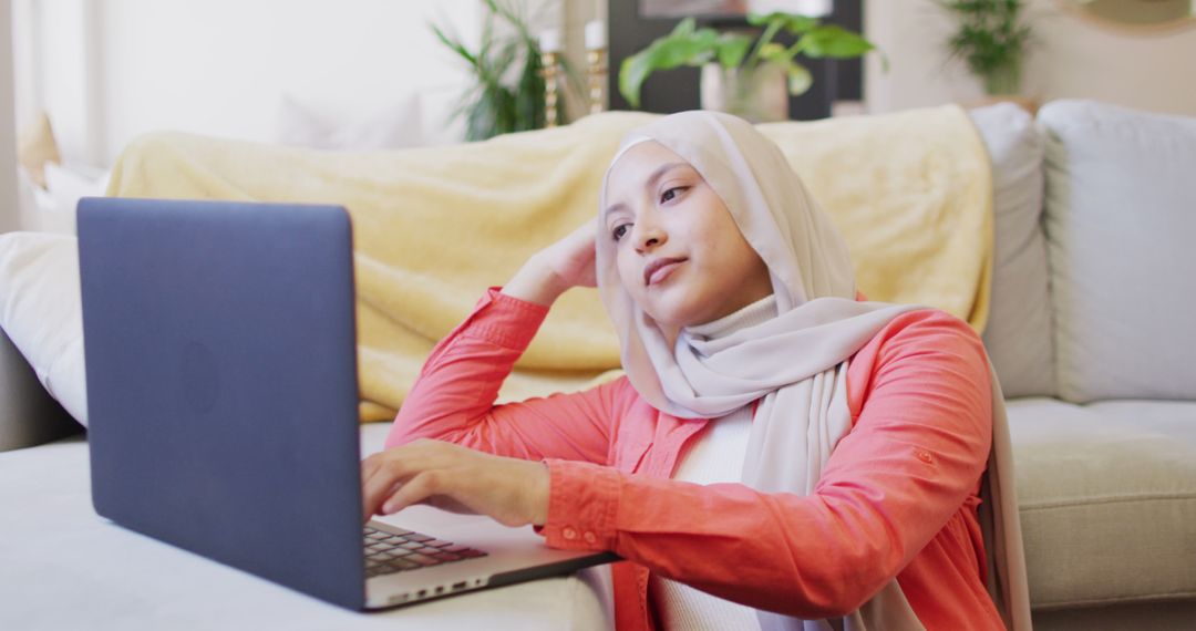 Muslim woman relaxing at home while using laptop on couch - Free Images, Stock Photos and Pictures on Pikwizard.com