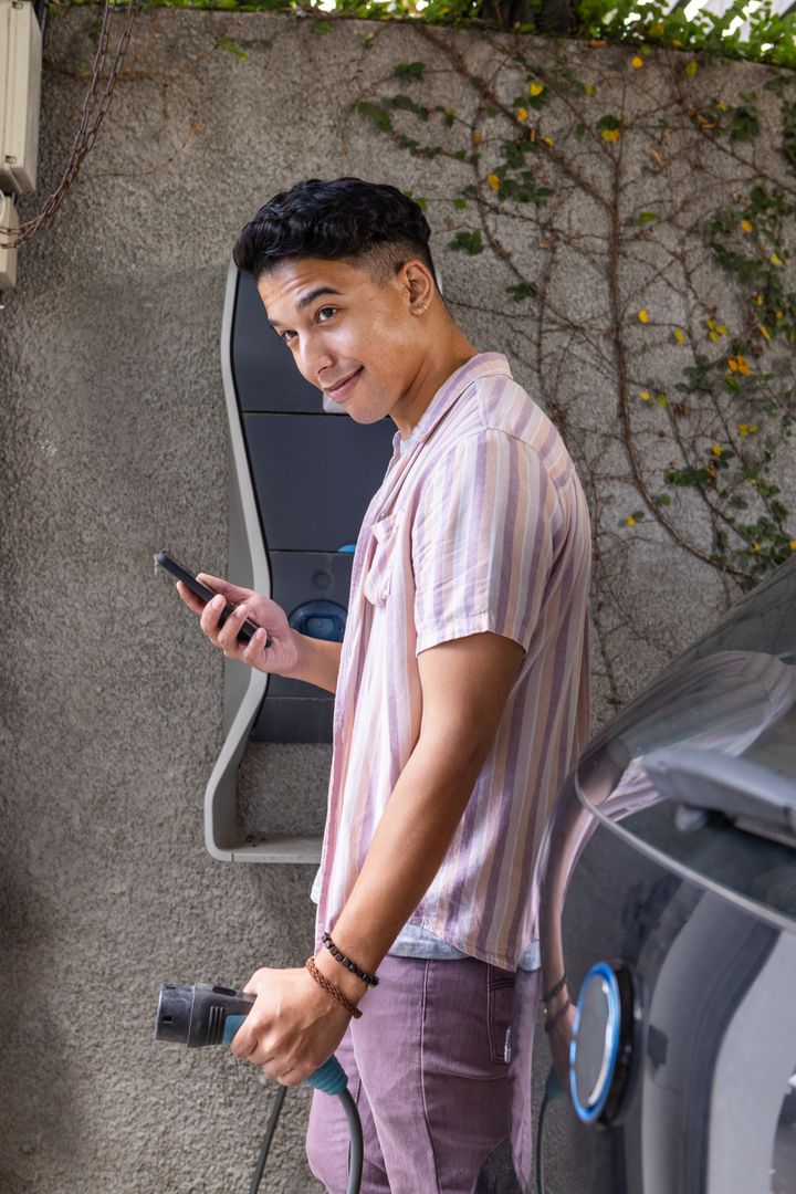 Man Charging Electric Car at Home Using Smartphone Connectivity
