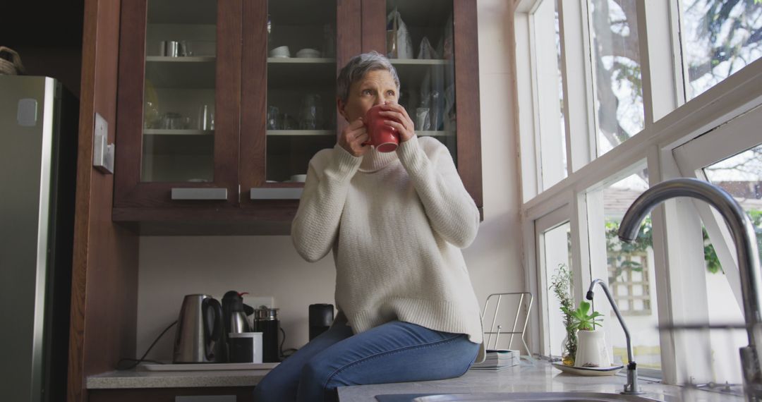 Relaxed Senior Woman Drinking Coffee by Kitchen Window - Free Images, Stock Photos and Pictures on Pikwizard.com