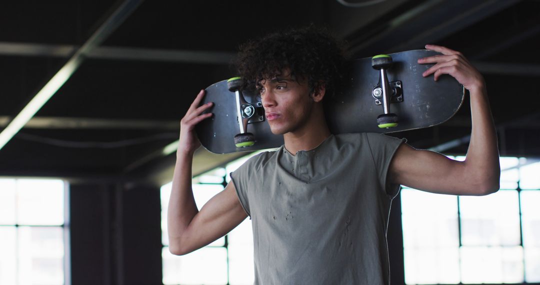 Young Man Holding Skateboard on Shoulders in Indoor Skate Park - Free Images, Stock Photos and Pictures on Pikwizard.com