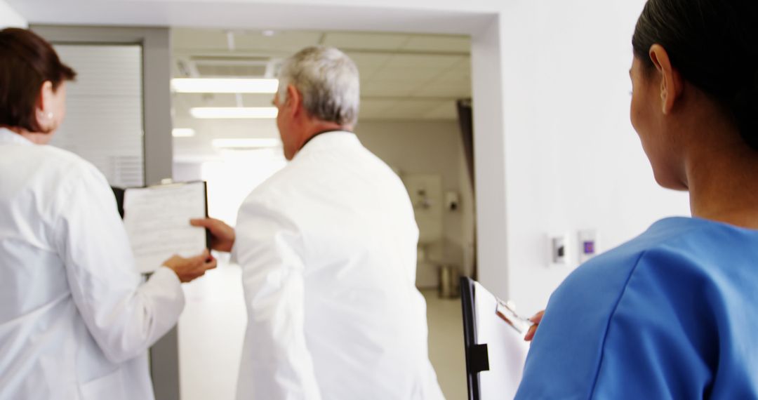 Medical Team Walking in Hospital Corridor, Discussing Patient Records - Free Images, Stock Photos and Pictures on Pikwizard.com