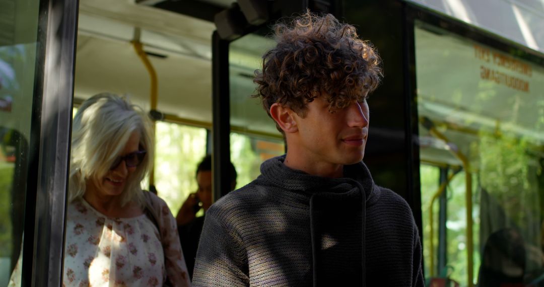 Young Man with Curly Hair Disembarking Bus in Sunlight - Free Images, Stock Photos and Pictures on Pikwizard.com