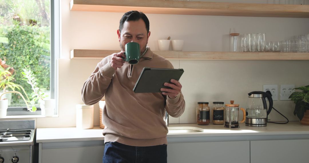 Mature Man Sipping Coffee and Using Tablet in Modern Kitchen