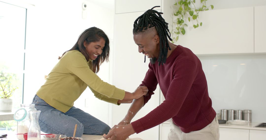 Diverse couple kneading dough together in bright modern kitchen