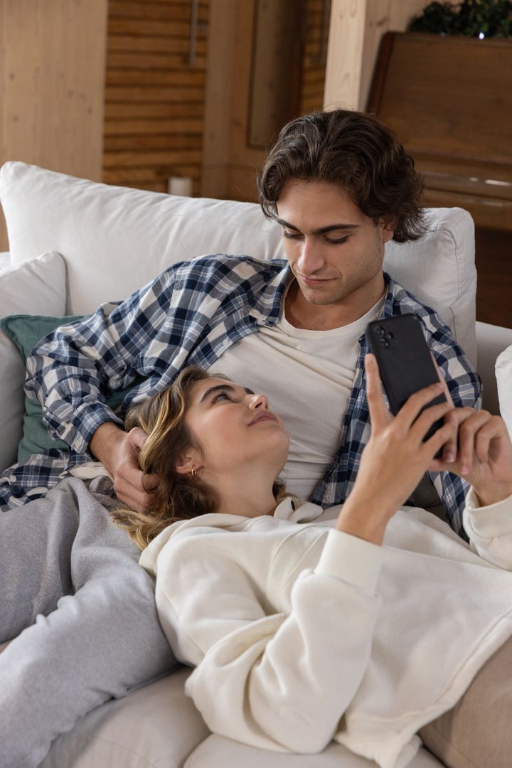 Romantic Couple Relaxing Together on Sofa with Smartphone