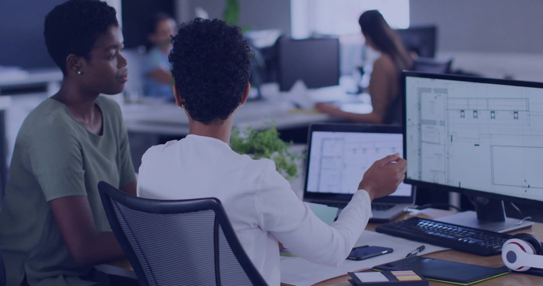 Colleagues Collaborating on Architectural Plans at Dual-Monitor Desk in Modern Office