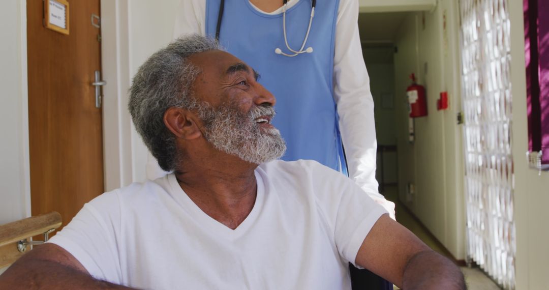 Senior Man Smiling While Being Helped in Wheelchair by Healthcare Worker