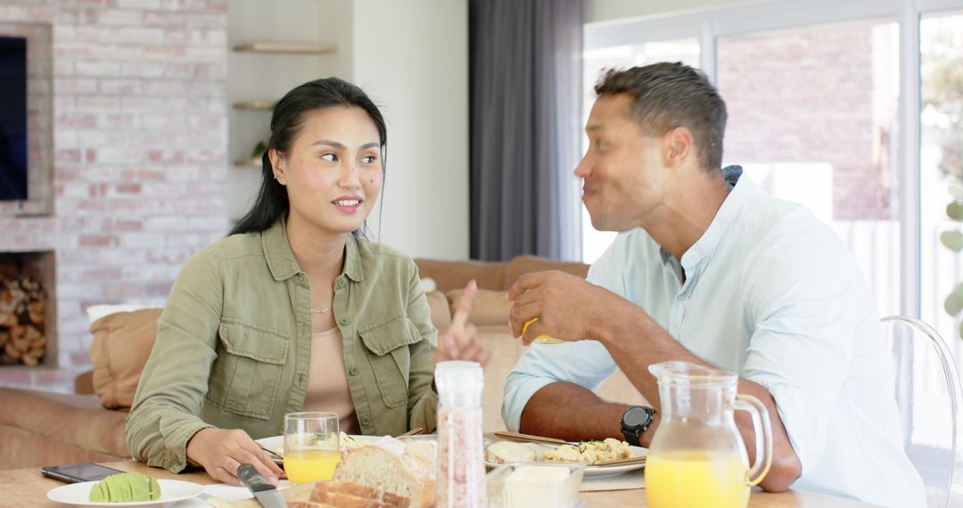 Couple sharing relaxed breakfast and chatting at sunlit dining table with orange juice