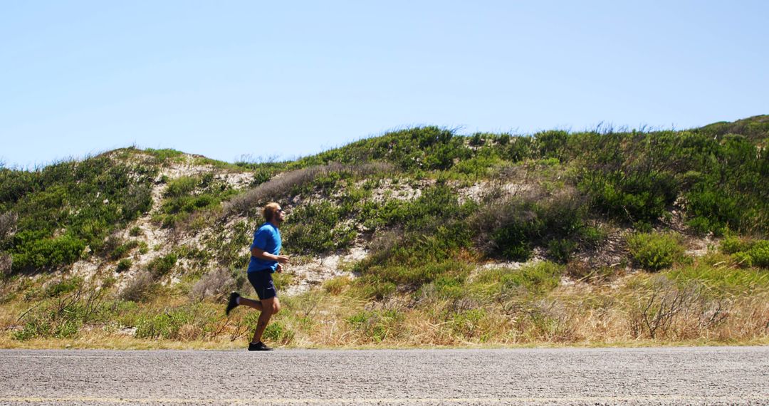 Man Running on Road by Coastal Hillside on Sunny Day - Free Images, Stock Photos and Pictures on Pikwizard.com