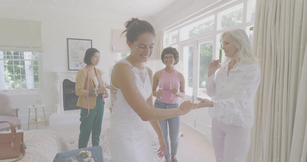 Bride trying on lace wedding gown with tailor and friends sharing champagne at home
