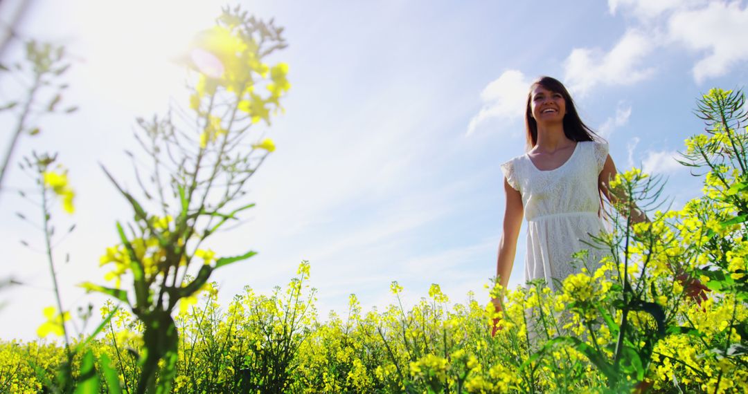 Woman in White Dress Walking Through Yellow Flower Field on Sunny Day - Free Images, Stock Photos and Pictures on Pikwizard.com