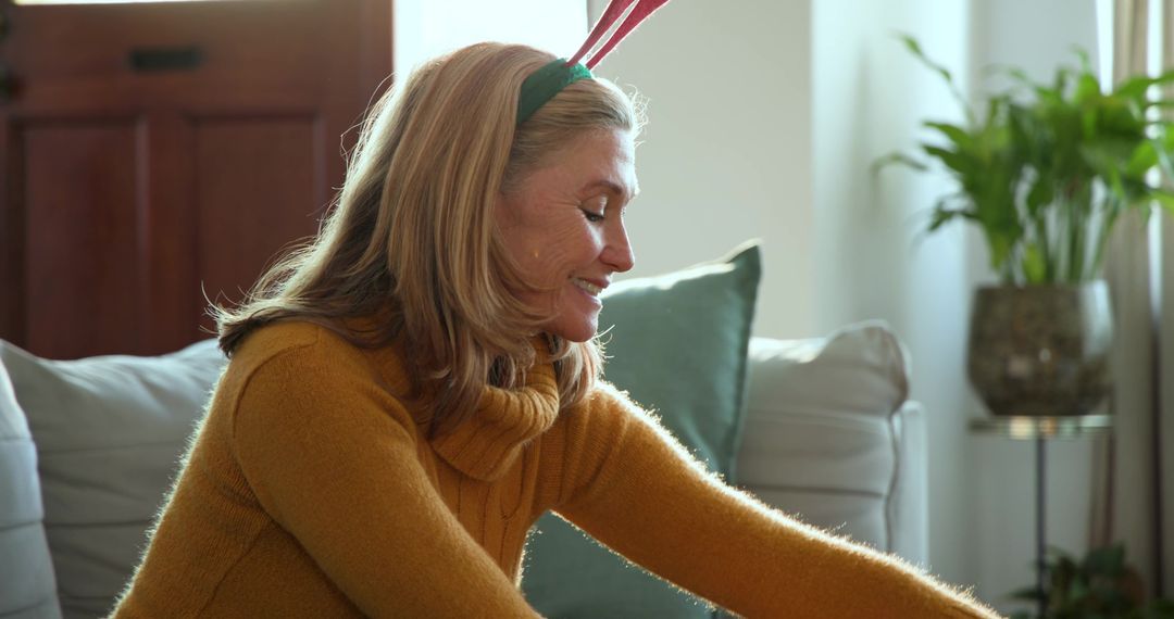 Smiling Mature Woman Wearing Green Headband with Red Antlers Relaxing on Couch