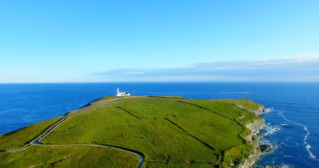 Cape with Lighthouse and Transparent Ocean Waters Below Clear Blue Sky