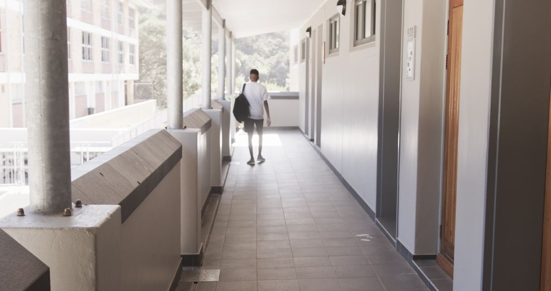 Youth Walking Down Dorm Hallway with Bag in Urban University