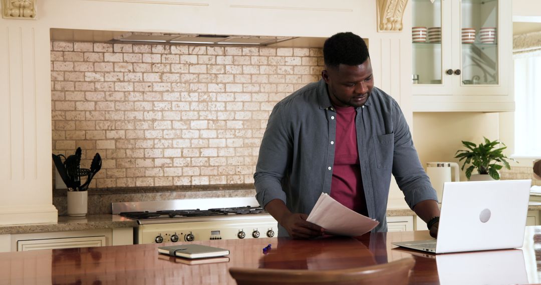 Man Working on Budget Plans in Home Kitchen with Laptop