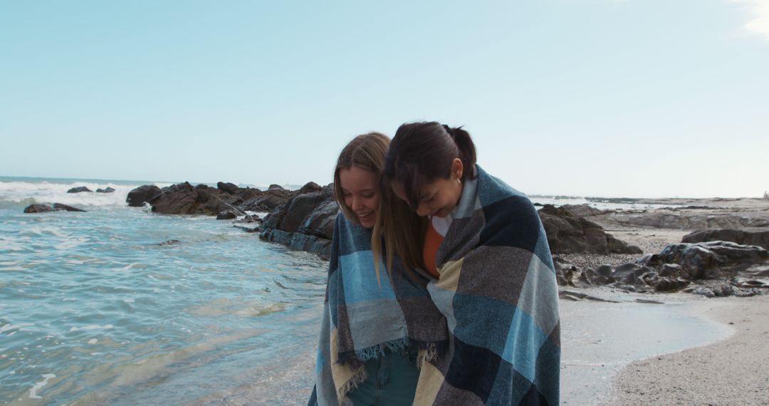 Two Women Enjoying a Peaceful Day at the Beach Wrapped in a Blanket - Free Images, Stock Photos and Pictures on Pikwizard.com